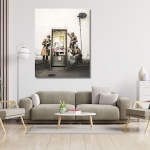 Puede incluir: Impresión artística enmarcada que representa una escena callejera con figuras interactuando con una cabina telefónica. La obra de arte presenta una paleta de colores apagados, con figuras que visten abrigos y sombreros. La cabina telefónica es el punto focal.