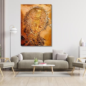 May include: Abstract artwork depicting a textured, golden-brown portrait of a person's face. The artwork is displayed on a wall above a grey sofa, with a modern lamp and chairs in the room. The painting has a unique, three-dimensional quality.