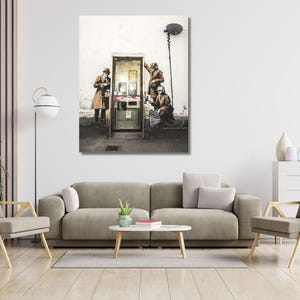 Puede incluir: Impresión enmarcada de una obra de arte callejero que representa a tres figuras interactuando con una cabina telefónica. La obra de arte está en tonos apagados, con las figuras vestidas con abrigos y sombreros. Una antena parabólica está montada arriba.