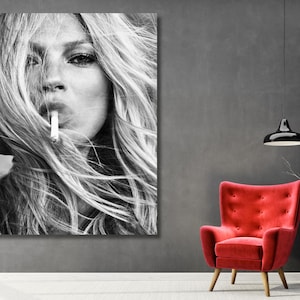 May include: A large rectangular black and white wall art print featuring a portrait of a person with long hair holding a cigarette to their lips. The artwork is displayed on a gray wall above a bright red armchair and two white vases.