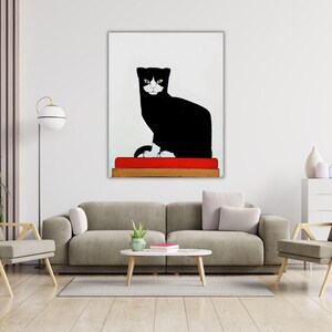 May include: A vertical wall art print featuring a stylized black and white cat with a white face and paws, sitting on a bright red rectangular cushion that rests on a wooden base, all set against a plain white background.