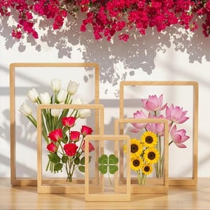 Pode incluir: Uma coleção de molduras de madeira com flores prensadas. As molduras contêm tulipas brancas, rosas vermelhas, flores de lótus rosa, girassóis amarelos e um trevo de quatro folhas. O fundo apresenta uma parede branca e flores vermelhas.