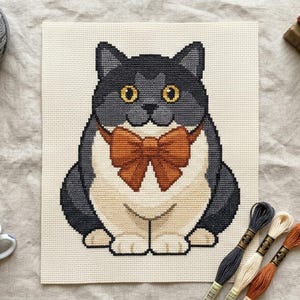 Peut inclure: Un motif de point de croix sur toile Aida blanche représentant un chat assis avec un pelage gris foncé, un poitrail et des pattes crème, et des yeux jaune vif. Le chat porte un grand nœud papillon orange-brun autour du cou.