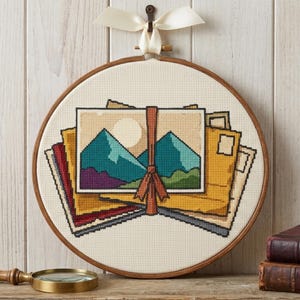 Peut inclure: Un tambour à broder circulaire en bois contenant un motif au point de croix représentant des enveloppes empilées et une carte postale avec un paysage de montagne et un soleil, liés par un ruban vertical et un nœud en tissu blanc.