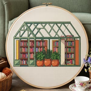 Puede incluir: Un bastidor de bordado circular de madera que contiene un patrón de punto de cruz de un invernadero. Dentro de la estructura verde hay estanterías de madera llenas de libros coloridos y tres plantas verdes en macetas de terracota.