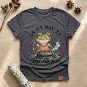 Puede incluir: Una taza de cerámica blanca con un asa negra y el texto "But First, Coffee" en negrita negra. La taza está llena de un líquido oscuro, probablemente café, y se encuentra sobre una superficie clara.