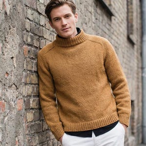 Könnte beinhalten: Ein senfgelber Rollkragenpullover mit langen Ärmeln. Der Pullover hat einen gerippten Saum und Bündchen. Die Person trägt ein schwarzes Hemd darunter und eine weiße Hose. Der Pullover ist aus Strickmaterial.