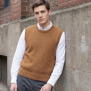 May include: A man wearing a brown knitted vest over a white collared shirt and gray pants. The vest has a ribbed hem and crew neck. The man is leaning against a concrete wall next to a brick wall.