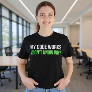 Puede incluir: Camiseta negra de cuello redondo con el texto blanco y verde "MY CODE WORKS I DON'T KNOW WHY". La persona lleva la camiseta en un entorno de oficina bien iluminado.