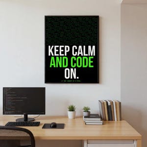 May include: A framed poster with the text "KEEP CALM AND CODE ON" in white and green against a black background. The top half of the poster features green code on a black background. The poster is displayed above a desk with a computer and accessories.