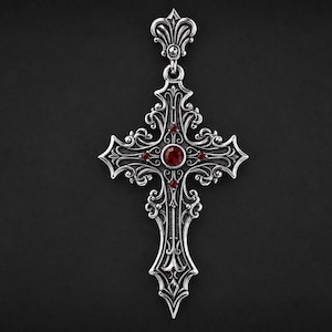 Könnte beinhalten: Ein silberfarbener Metall-Kreuzanhänger mit aufwendigen Schnörkeln und Filigranverzierungen. In der Mitte des Kreuzes befindet sich ein runder, dunkelroter Edelstein, ergänzt durch vier kleinere rote Steine, die kreuzförmig um die Mitte angeordnet sind.