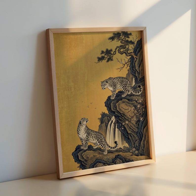 A traditional East Asian sumi-e style painting featuring two snow leopards on rocky cliffs beside a flowing waterfall, with a twisted pine branch and white plum blossoms cascading from above, set against a warm luminous gold leaf background with small birds in the distance in muted earthy tones.