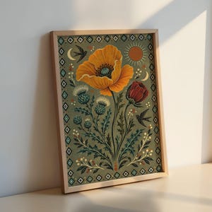 May include: A framed rectangular wall art print featuring a large orange poppy, a red flower, and green thistle plants on a sage green background. The illustration includes two black birds, a sun, and a crescent moon, all enclosed by a geometric diamond border.