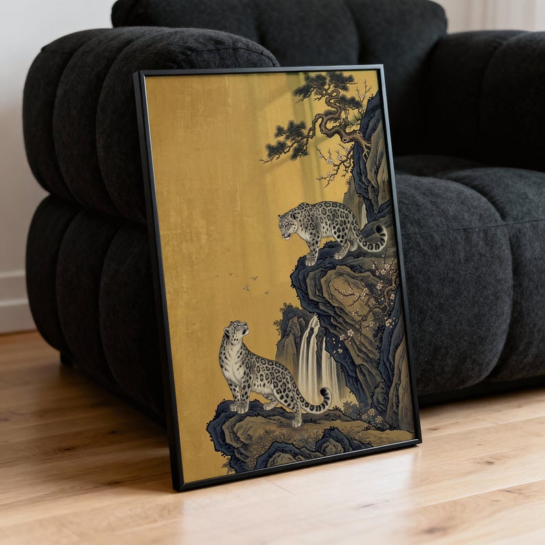 A traditional East Asian sumi-e style painting featuring two snow leopards on rocky cliffs beside a flowing waterfall, with a twisted pine branch and white plum blossoms cascading from above, set against a warm luminous gold leaf background with small birds in the distance in muted earthy tones.