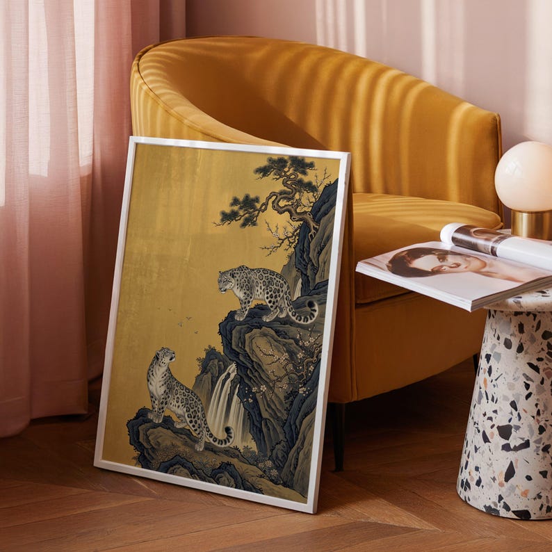 A traditional East Asian sumi-e style painting featuring two snow leopards on rocky cliffs beside a flowing waterfall, with a twisted pine branch and white plum blossoms cascading from above, set against a warm luminous gold leaf background with small birds in the distance in muted earthy tones.