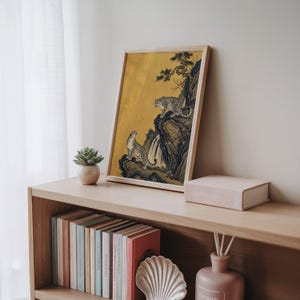 A traditional East Asian sumi-e style painting featuring two snow leopards on rocky cliffs beside a flowing waterfall, with a twisted pine branch and white plum blossoms cascading from above, set against a warm luminous gold leaf background with small birds in the distance in muted earthy tones.