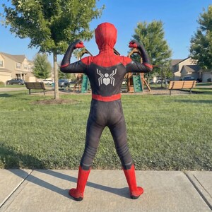 May include: A full-body Spider-Man costume, featuring a red and black color scheme. The costume includes a mask, and the Spider-Man logo is visible on the back. The person is flexing their arms, showcasing the costume's design.