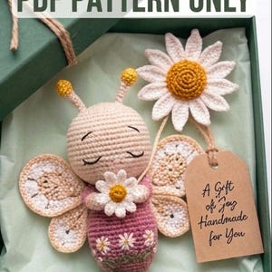 May include: A handmade crochet butterfly and daisy set in a gift box. The butterfly is light pink and beige with a daisy on its chest. The box includes a tag that reads "A Gift of Joy Handmade for You". The text "PDF PATTERN ONLY" is at the top.