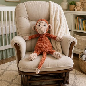 May include: A plush monkey toy crafted from chunky, rust-orange and cream-coloured yarn. The stuffed animal features a round face, small ears, long arms and legs, and a long tail, all with a soft, textured appearance and black plastic eyes.