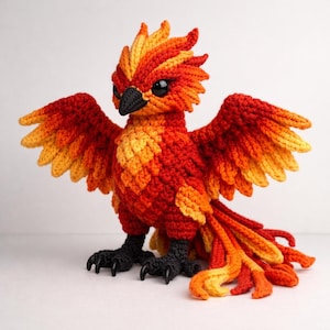 Peut inclure: Un phénix au crochet fait à la main, aux teintes vives de rouge, orange et jaune. L'oiseau a les ailes déployées, une tête détaillée avec un bec et des yeux noirs, et des griffes noires. Le travail artisanal présente un aspect texturé et emplumé.