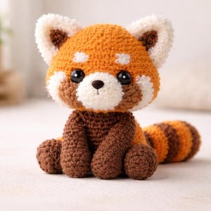 May include: A handmade crochet red panda plush toy. The plush features a vibrant orange body with white and brown accents, including a fluffy tail and ears. The red panda has black eyes and a brown nose, and is sitting upright.