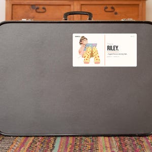 May include: A rectangular sticker featuring an illustration of a person with brown hair wearing yellow pants with red heart patterns, holding a tablet. The text reads: ADHD is RILEY. ...hyperfocus, wrong tab. The sticker is centered on a dark gray suitcase.