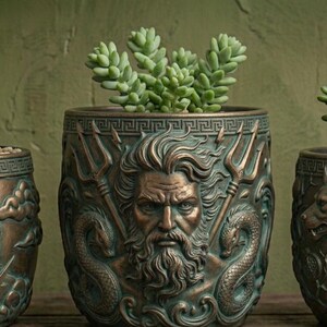 May include: Three cylindrical bronze-toned planters featuring relief carvings of bearded male figures. Each pot contains a small green succulent plant. The designs include mythological motifs such as tridents, snakes, and canine heads, with a Greek key pattern border along the top rim of each vessel.