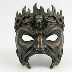 Può includere: Maschera color bronzo con un'espressione feroce, con una corona di fiamme, serpenti e un lupo ringhiante. La maschera ha fori per gli occhi e una barba dettagliata, con iscrizioni dall'aspetto antico. Un pezzo decorativo.