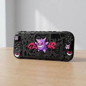 May include: A black handheld gaming console case featuring a pixelated purple ghost character in the centre with the text GENGAR in bright pink. The case is decorated with various black and grey ghost-themed graffiti patterns and icons.
