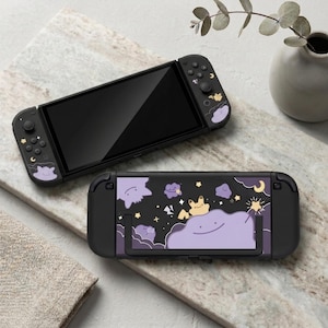 Könnte beinhalten: Zwei schwarze Nintendo Switch Konsolen mit individuellen lila und gelben Charakterdesigns. Eine Konsole ist geöffnet und zeigt den Bildschirm, während die andere die Rückseite mit einem passenden Design zeigt. Das Design zeigt Cartoon-Charaktere, Wolken und Sterne.