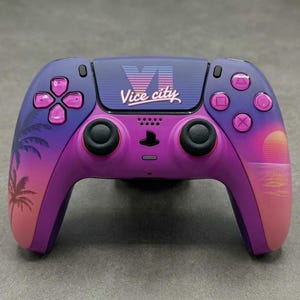 Puede incluir: Un mando de videojuegos inalámbrico con un acabado en degradado morado y rosa, siluetas de palmeras en el agarre izquierdo y un gráfico de atardecer a la derecha. El panel táctil central muestra el texto VI Vice City en una fuente estilizada.
