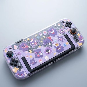 May include: A handheld gaming console featuring a light purple protective skin decorated with various purple Gengar character stickers, including images of the creature eating desserts, sleeping, and smiling, alongside small stars and Poké Ball icons.