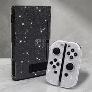 May include: A black Nintendo Switch console and Joy-Con controllers with a starry design. The console has a black background with white stars. The Joy-Con controllers are white with black buttons and a similar starry pattern.