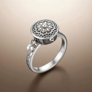 Puede incluir: Un anillo plateado con un diseño floral detallado en la parte superior, con un pequeño acento de perla. El anillo tiene un diseño de rueda giratoria y una perla colgante. La banda está grabada con escritura.