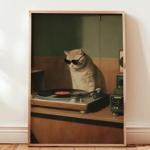 以下が含まれることがあります： サングラスをかけた猫がレコードプレーヤーの近くに座っている額入りのプリント。猫は薄いオレンジ色で、黒いサングラスをかけています。レコードプレーヤーはシルバーとブラックで、黒いレコードが付いています。背景はくすんだ緑と茶色です。