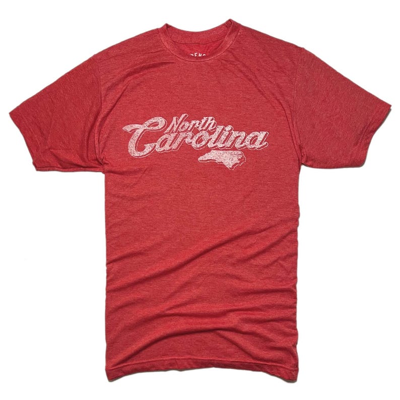 K&ouml;nnte beinhalten: Rotes T-Shirt mit dem Text "North Carolina" in verblichener wei&szlig;er Schrift und einer wei&szlig;en Umrisslinie des Bundesstaates. Das Shirt hat kurze &Auml;rmel und einen Rundhalsausschnitt.