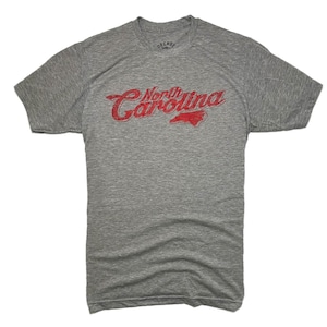 K&ouml;nnte beinhalten: Ein meliertes graues T-Shirt mit dem Text "North Carolina" in verblichener roter Schrift und einer roten Umrisszeichnung des Bundesstaates. Das Shirt besteht aus einem weichen, bequemen Material.