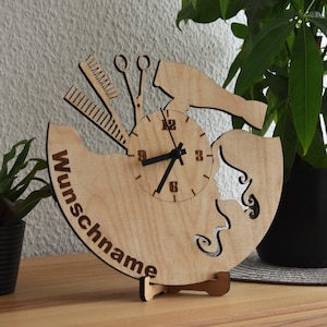 Puede incluir: Reloj de madera con temática de peluquería. El reloj presenta un diseño de peine, tijeras y secador de pelo. La esfera del reloj tiene manecillas y números negros. La palabra "Wunschname" está escrita en el reloj. El reloj está sobre un soporte de madera.