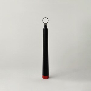 May include: A pottery trimming tool featuring a long, black, faceted handle with a red base and a circular metal wire loop at the top. The tool is designed for carving and shaping clay, showcasing a sleek, geometric design with a functional metal tip.