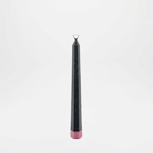 Puede incluir: Una vela alta y negra con una superficie texturizada y una base rosa. La vela tiene un lazo de metal plateado en la parte superior. La vela está de pie sobre un fondo blanco.