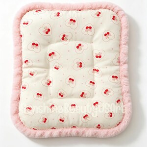 May include: A rectangular pet bed with a cream-colored surface featuring a pattern of pink hearts and cherries. The bed has a soft, pink, fluffy border. The bed is designed for small pets.