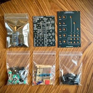 Può includere: Un assortimento di componenti elettronici per un progetto fai-da-te, tra cui circuiti stampati, resistenze e potenziometri, disposti su una superficie di legno. I componenti sono confezionati in sacchetti di plastica trasparente e includono una piccola scheda blu.
