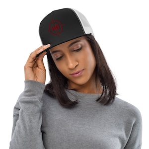 May include: Black and white trucker hat with a red target logo. The hat features a black front panel with the logo, a white mesh back, and a flat brim. The hat is being held by a person.
