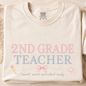 Puede incluir: Una camiseta de color crema con el texto 2ND GRADE TEACHER en rosa y azul. Debajo del texto hay un gráfico de un lápiz, un lazo rosa y una estrella conectados por una línea discontinua, con las palabras smart, sweet, and school-ready impresas debajo.