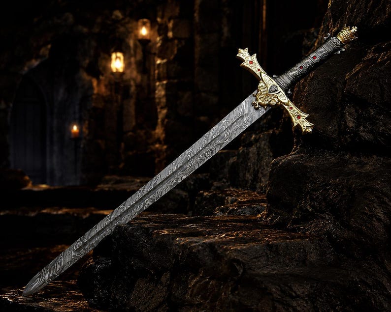 May include: A sword with a patterned Damascus steel blade and a gold-coloured crossguard featuring red accents. The handle is black with gold-coloured metal details, including a crown-shaped pommel at the end of the grip.