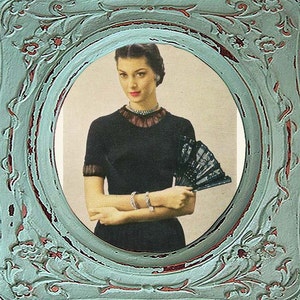 Può includere: Una donna con un vestito nero con un colletto di pizzo tiene un ventaglio bianco e nero. Indossa una collana di perle e un braccialetto. L'immagine è incorniciata in una cornice rozzamente color verde acqua e rosso.