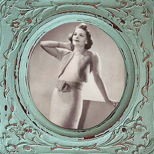 May include: A black and white photo of a woman wearing a knitted cardigan and skirt, framed in a distressed teal oval frame.