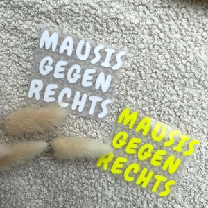 Könnte beinhalten: Zwei Aufbügelbilder auf einer strukturierten Oberfläche. Ein Aufkleber zeigt den weißen Schriftzug MAUSIS GEGEN RECHTS in einer fetten, abgerundeten Schriftart. Der zweite Aufkleber zeigt denselben Text in leuchtendem Neongelb auf transparenter Folie.