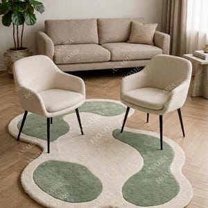 Könnte beinhalten: Moderne Wohnzimmereinrichtung mit beigem Sofa, zwei cremefarbenen Sesseln mit schwarzen Beinen und einem einzigartigen Teppich mit grünen und cremefarbenen organischen Formen. Eine Topfpflanze setzt einen natürlichen Akzent.