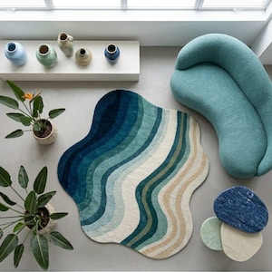 Könnte beinhalten: Draufsicht auf einen modernen Wohnraum. Ein wellenförmiger Teppich in Blau- und Beigetönen liegt neben einem türkisfarbenen Sofa. Dekorative Vasen säumen ein Regal, und Topfpflanzen sorgen für Grün. Ein Satz Untersetzer aus Stein vervollständigt die Szene.